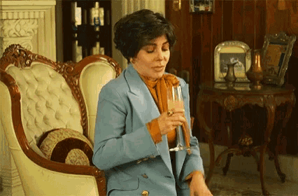 a woman in a blue suit is sitting in a chair holding a glass of wine