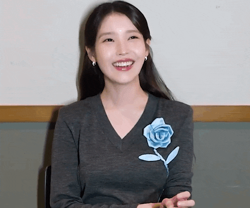 a woman wearing a grey sweater with a blue flower on the front is smiling