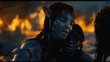 a woman with a blue face is hugging another woman with a fire in the background