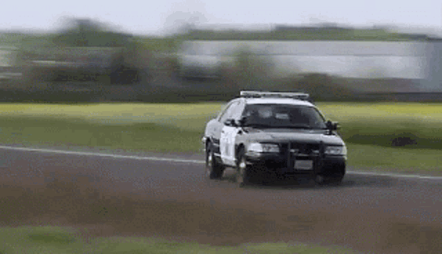 a police car is driving down a road with a field in the background .