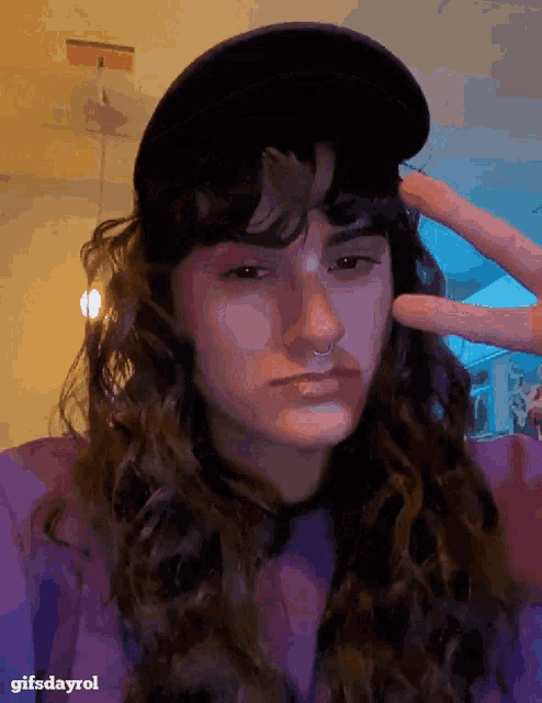 a woman wearing a black hat and a purple shirt is giving a peace sign
