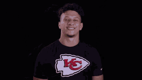 a man is wearing a black t-shirt with a chiefs logo on it and smiling .