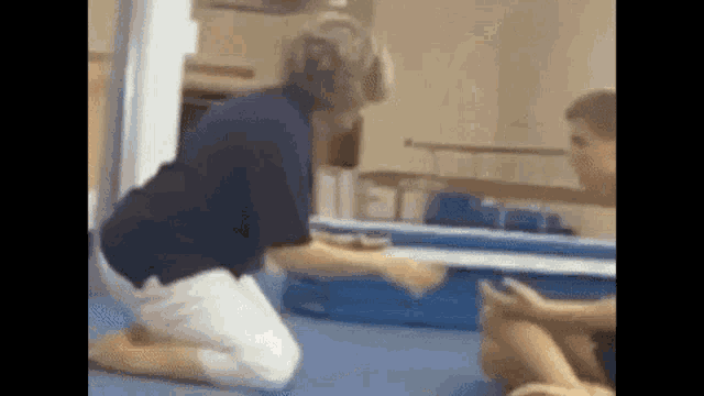 a woman is kneeling down next to a boy on a gymnastics mat .