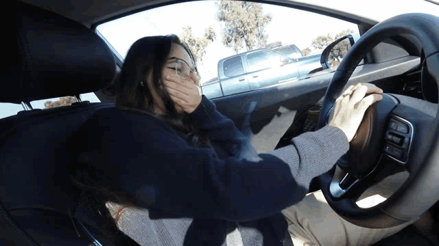 a woman driving a car with her hand over her mouth