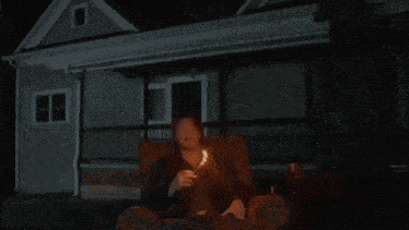 a man is sitting in front of a house that is on fire .