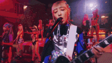 a woman is playing a guitar and singing into a microphone