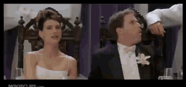 a bride and groom are sitting at a table in front of a movie clip