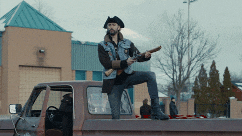 a man in a pirate hat is holding a gun on the back of a truck