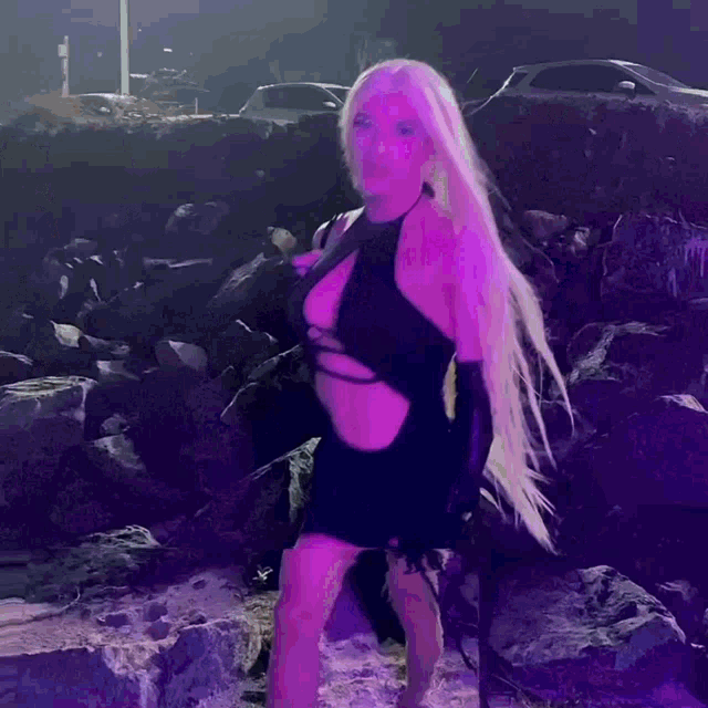 a woman with long blonde hair is standing in front of a rock wall