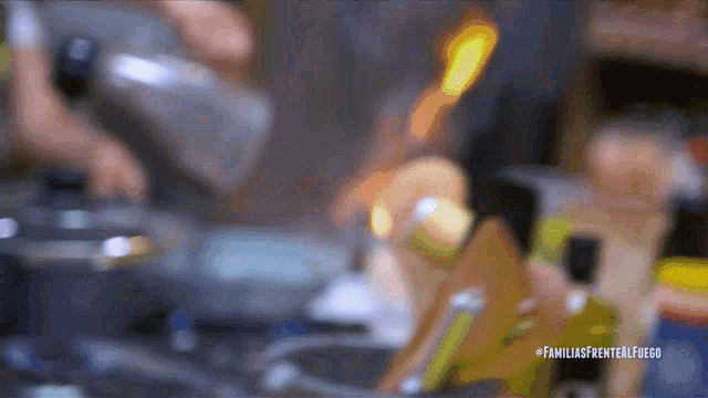 a blurred image of a person cooking with the hashtag familiasfrentealfuego on the bottom