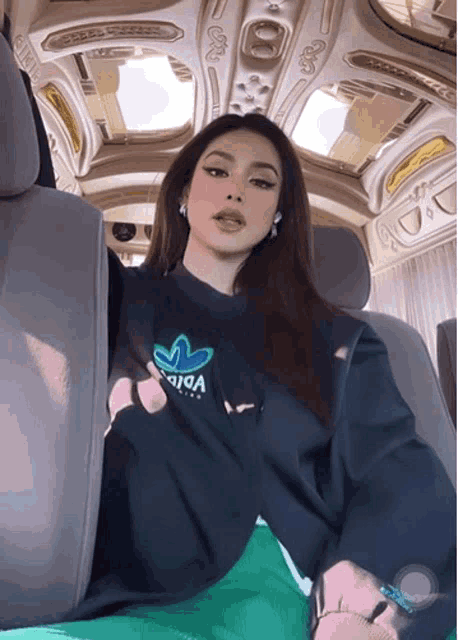 a woman wearing a black adidas sweatshirt is sitting in a car