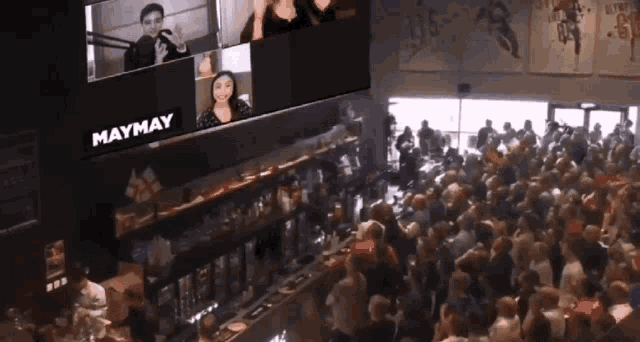 a crowd of people are gathered in front of a large screen that says maymay on it