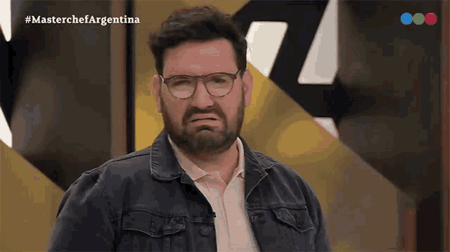 a man with glasses and a beard is making a face in front of a masterchef argentina sign