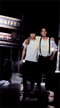 two men are singing into microphones on a stage and the word k-code is on the bottom right