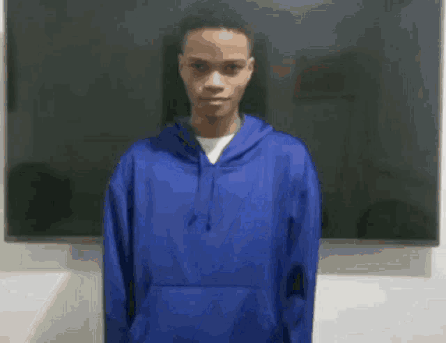 a young man wearing a blue hoodie is standing in front of a blackboard