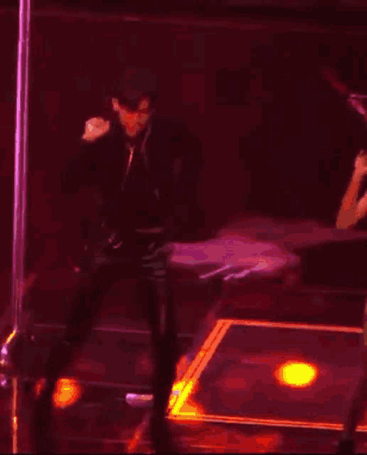 a man is dancing on a stage in a dark room with a pink pole in the background .