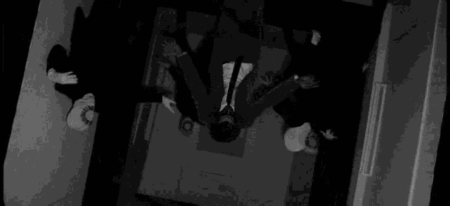 a black and white photo of a man in a suit and tie standing upside down in a dark room .