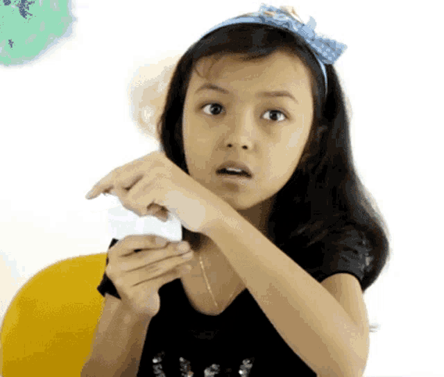 a young girl wearing a headband and a black shirt is holding a white object