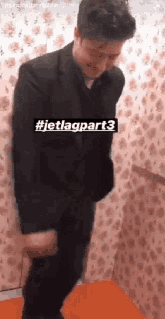 a man in a suit is standing in a room with a floral wallpaper .
