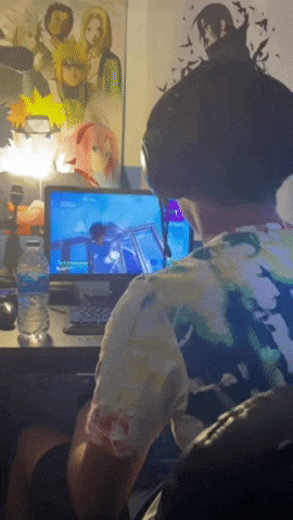 a man is playing a video game on a computer with a poster of naruto on the wall behind him