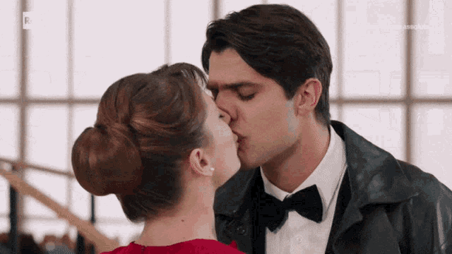 a man in a bow tie kisses a woman in a red top