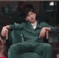 a man in a green suit is sitting in a chair covering his face .