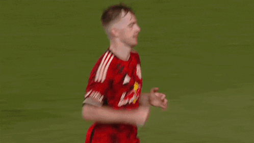 a soccer player wearing a red and black jersey with a bull on it is running on the field .