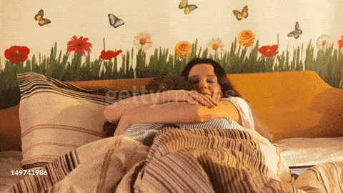 a woman hugging a man in a bed with a wall with flowers and butterflies