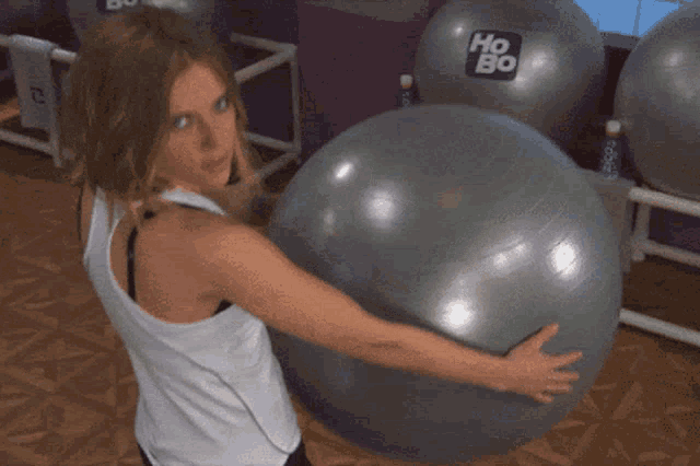 a woman in a white tank top is hugging a gray exercise ball with the word ho on it