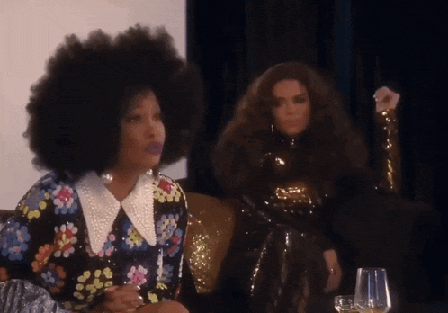 two women are sitting on a couch one has a large afro