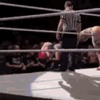 a referee is standing in the middle of a wrestling ring watching two wrestlers wrestling .