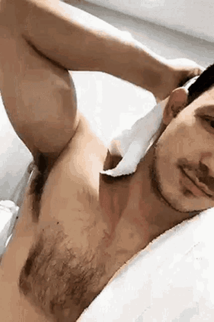 a shirtless man with a beard is laying on a bed with a towel around his neck .