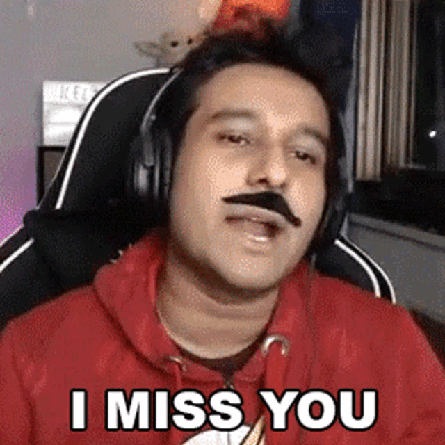 a man with a mustache and headphones is saying `` i miss you '' while sitting in a chair .