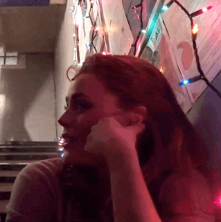 a woman is sitting in front of a wall with christmas lights hanging on it