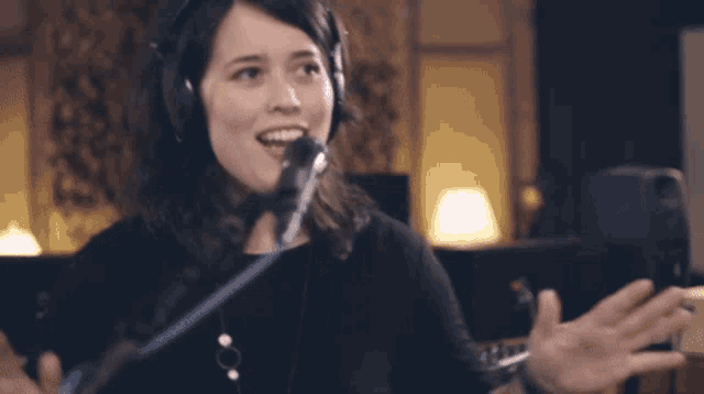 a woman wearing headphones and a necklace sings into a microphone