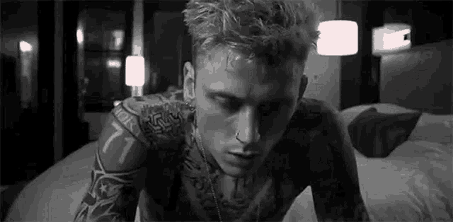 a black and white photo of a man with tattoos on his arms and chest laying on a bed .