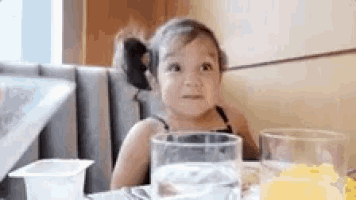 a little girl is sitting at a table with a glass of water and juice .