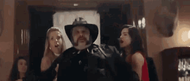 a man with a beard and a hat is pointing at the camera while two women look on .
