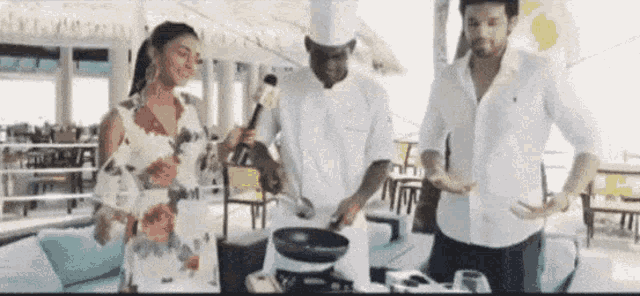 a woman is talking into a microphone while a man and a chef are cooking .
