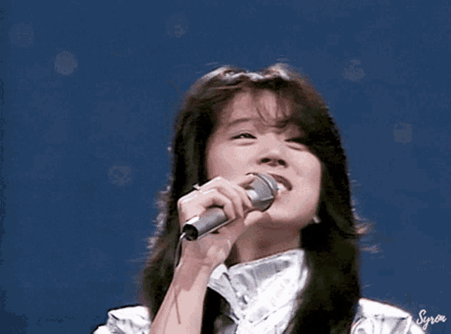 a woman is singing into a microphone with a blue background .