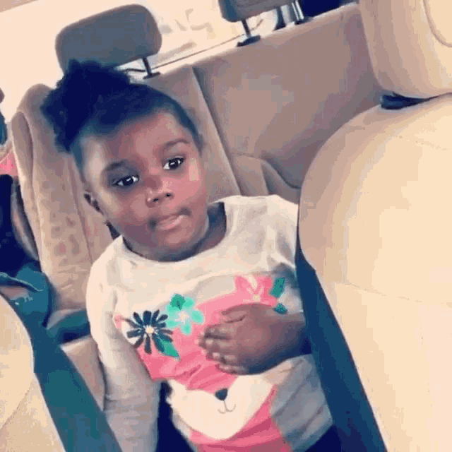 a little girl is sitting in the back seat of a car and looking at the camera .