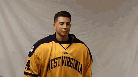 a man in a yellow west virginia jersey is holding a hockey stick