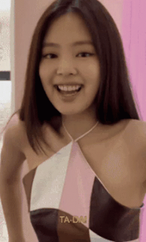 a woman wearing a halter top is smiling and looking at the camera while standing in front of a pink wall .