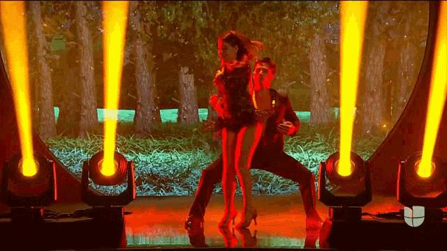 a man and a woman are dancing in front of a forest