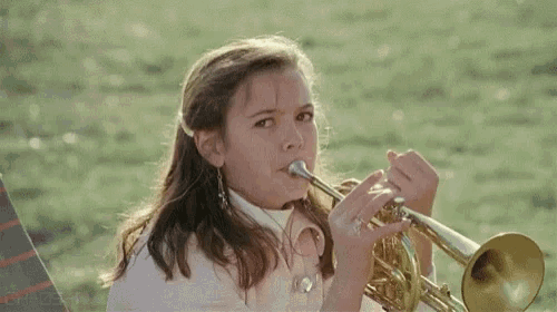 a young girl is playing a trumpet in a field and looking at the camera .