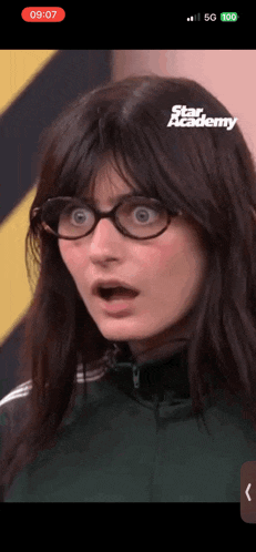 a woman wearing glasses and a green jacket is on a star academy advertisement