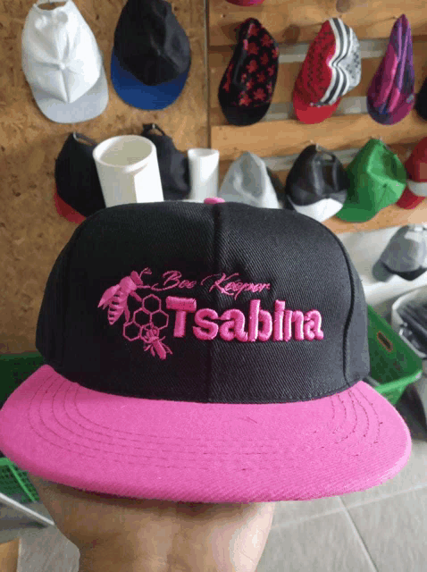 a person is holding a black and pink baseball cap with the name tsabina on it