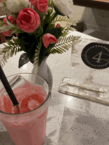 a glass of pink liquid sits on a table next to a vase of flowers