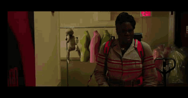 a woman is standing in a room with a red exit sign above her