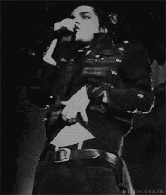 a black and white photo of a man singing into a microphone with jetblackfeeling written below him